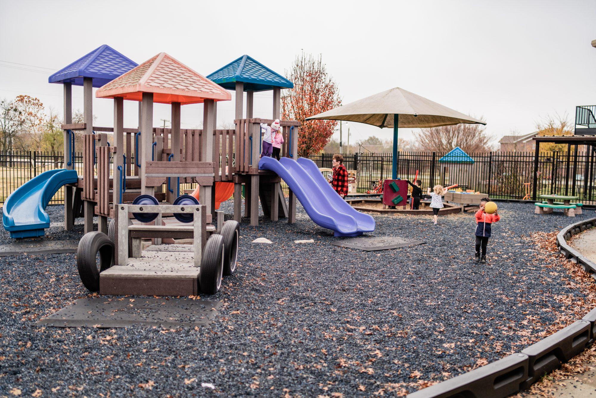 Playground equipment with several slides, swings, sand pit, tricycles and rubber mulch.